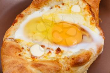 Ajarian khachapuri (Georgian cheese pastry), filled with cheese and topped with a soft-boiled egg and butter on ceramic plate close up