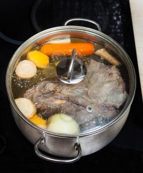 boiling of beef broth with seasoning vegetables in pan on glass ceramic cooker