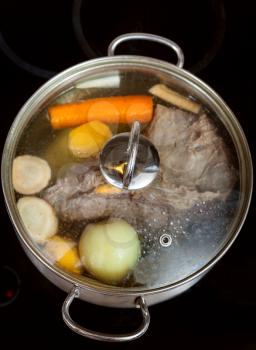cooking of beef broth with seasoning vegetables in pan on glass ceramic cooker