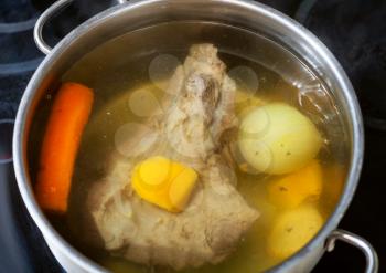 beef broth with seasoning vegetables in open pan on glass ceramic cooker