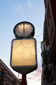 illuminated round street clock and blank advertising billboard in evening