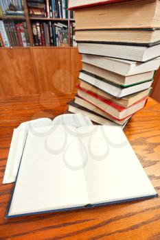 stack of books and two open blank and blur font books close up on wooden table near bookcases