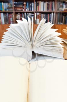 fanned open book and blank book close up on wooden table near bookcases
