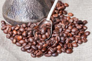 roasted coffee beans and copper coffee pot with spoon close up on sackcloth