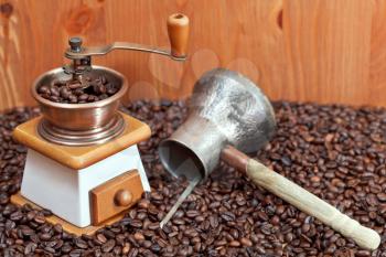 retro manual coffee grinder and copper pot on many roasted coffee beans near wooden wall