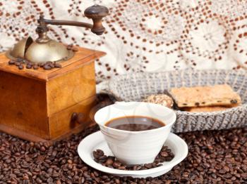 mug of coffee and roasted coffee beans with retro wooden manual mill, biscuit, openwork napkin