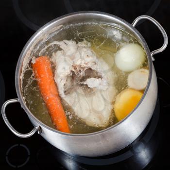 top view of boiling chicken broth with seasoning vegetables in steel pan on glass ceramic cooker
