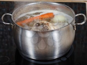simmering chicken soup in steel pot on glass ceramic cooker close up