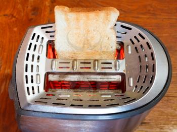 one toasted slice of bread on hot metal toaster on wooden table