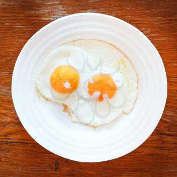 white plate with two fried eggs on wooden table