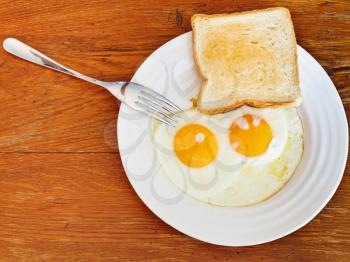 fresh toast and two fried eggs on white plate on wooden table
