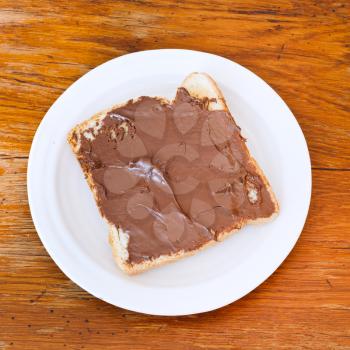 sweet sandwich from fresh toast with chocolate spread on white plate at wooden table