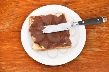 top view of fresh toast with chocolate spread on white plate, table knife on wooden table