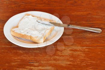sandwich from toast and soft cheese with herbs on white plate, table knife on wooden table