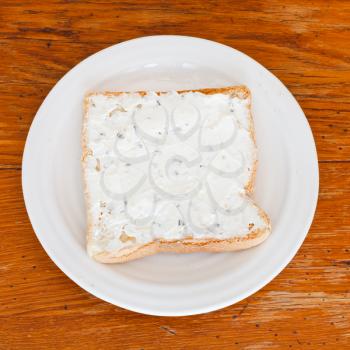 sandwich from toast and soft cheese with herbs on white plate on wooden table