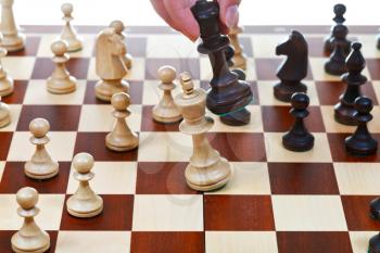 hand with black king beats white king on chessboard in chess game