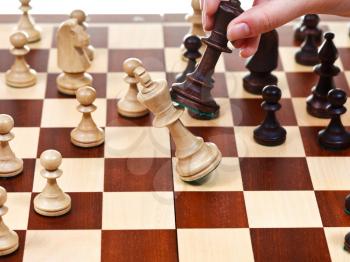 hand with black king throws white king on chessboard in chess game
