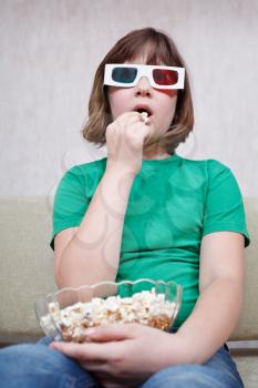 Girl watching TV movies in anaglyph stereo glasses and eating popcorn