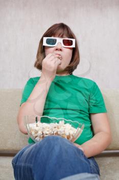 Girl watching TV movies in anaglyph 3D stereo glasses and eating popcorn at home