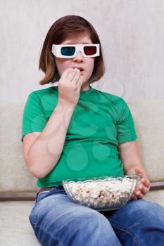 Girl watching TV in anaglyph 3D stereo glasses and eating popcorn it home