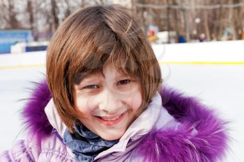 smiling girl in down-padded coat close-up on rink in sunny winter day