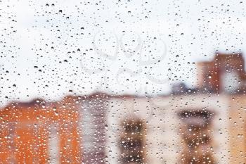 raindrops on home glass window with city buildings background