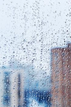raindrops on glass window with winter city buildings background