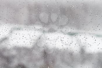 raindrops on glass window with winter urban background