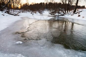 icebound riverbank of forest river at winter sunset
