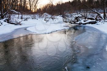 icebound banks of forest pond at winter sunset