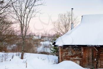 snowcovered wooden house in country at pink winter sunset