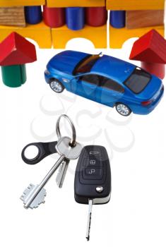 above view of door keys, vehicle key, new blue car model close up and wooden block toy house isolated on white background