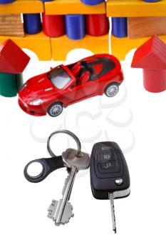 door keys, vehicle key, new red car model close up and wooden block toy house isolated on white background