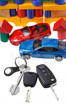 above view of door keys, vehicle keys, two car models and wooden block toy house isolated on white background