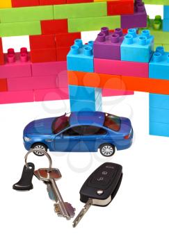 above view of door key, vehicle keys, blue model car and plastic block house isolated on white background