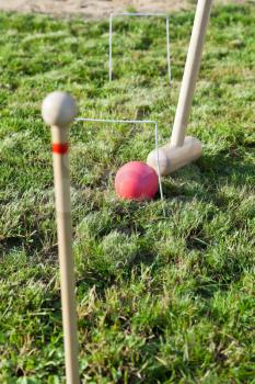 hitting through hoop by red ball game of croquet on green lawn in summer day