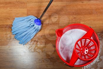 cleaning of wooden floors and red bucket with washing water