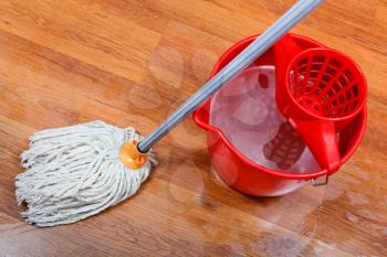 cleaning of wet floors by mop and red bucket with washing water