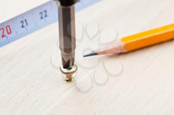 measuring tape, pencil and screwdriver wraps screw in wooden board