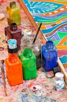 paintbrushes, bottles with color pigments and ornament on silk