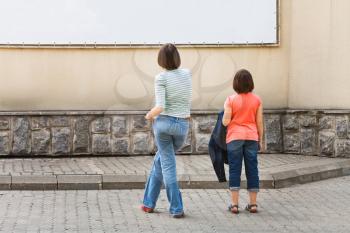 two girls look at advertising banner on house wall