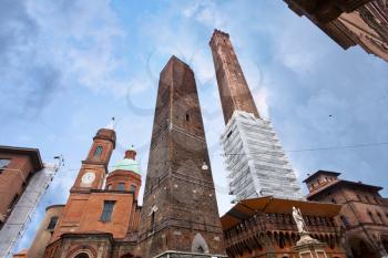 palace and two towers and statue of Saint Petronius under cloudy sky in Bologna, Italy
