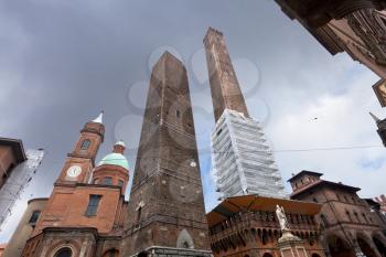palace and two towers and statue of Saint Petronius under grey sky in Bologna, Italy