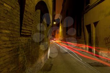 stone medieval street in Bologna and car red headlights at night, Italy