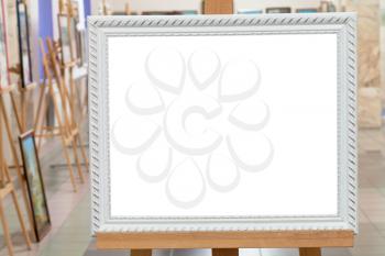 white picture frame with white cut out canvas on easel in art gallery hall
