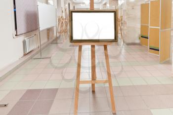 golden wood picture frame with white cut out canvas on easel in art gallery hall