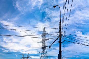 Electric power transmission under white cirrus clouds in blue summer sky