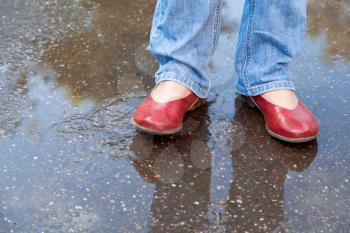 legs in blue jeans and red shoes in autumn rainy puddle