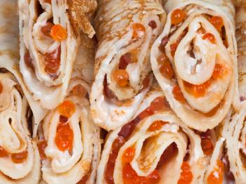 food background from pancakes rolls with red caviar close up