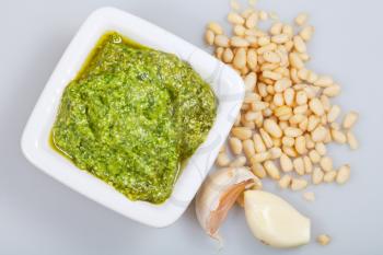 top view on italian pesto with pine nuts and garlic cloves on grey background